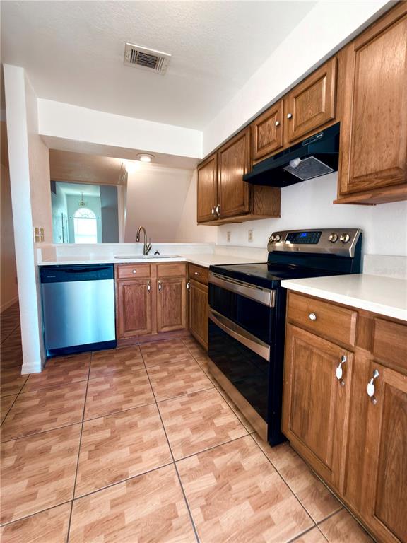 A kitchen features oak cabinets, stainless steel appliances, white countertops, and light-colored tiled flooring — 3136 ENCLAVE CT, KISSIMMEE, FL