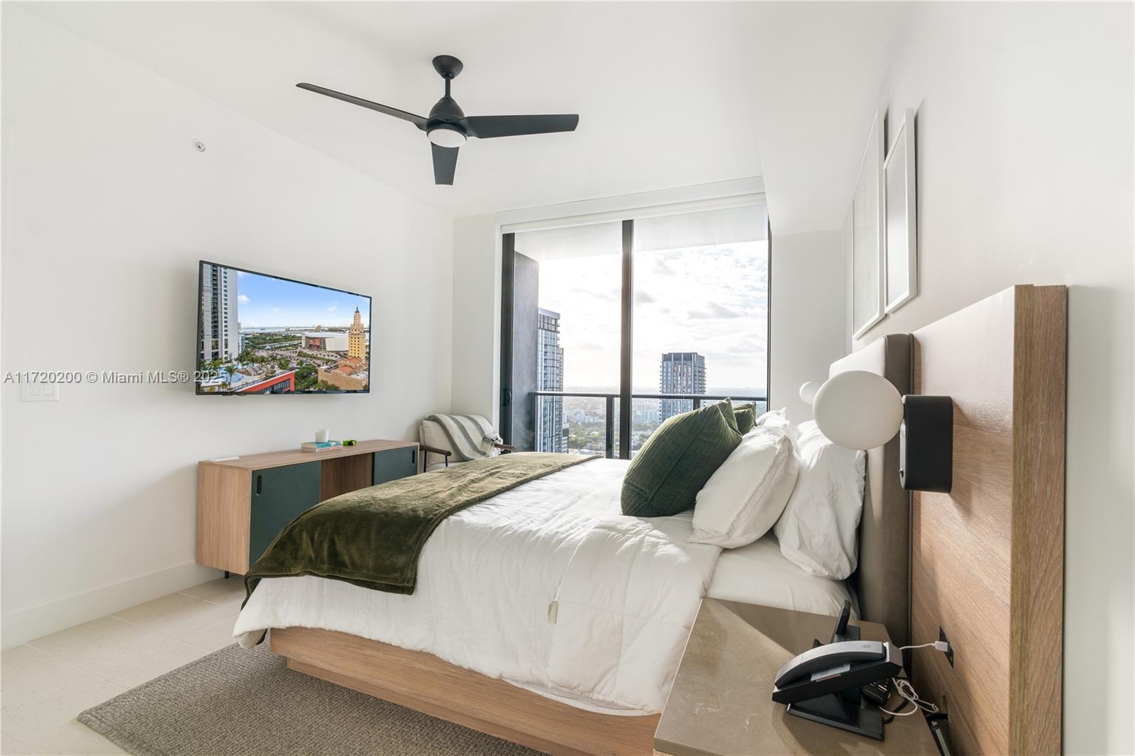 A modern bedroom features a bed, wall-mounted television, ceiling fan, and floor-to-ceiling windows with views — 601 NE 1 AVE # 3604, Miami FL 33132, MIAMI, FL