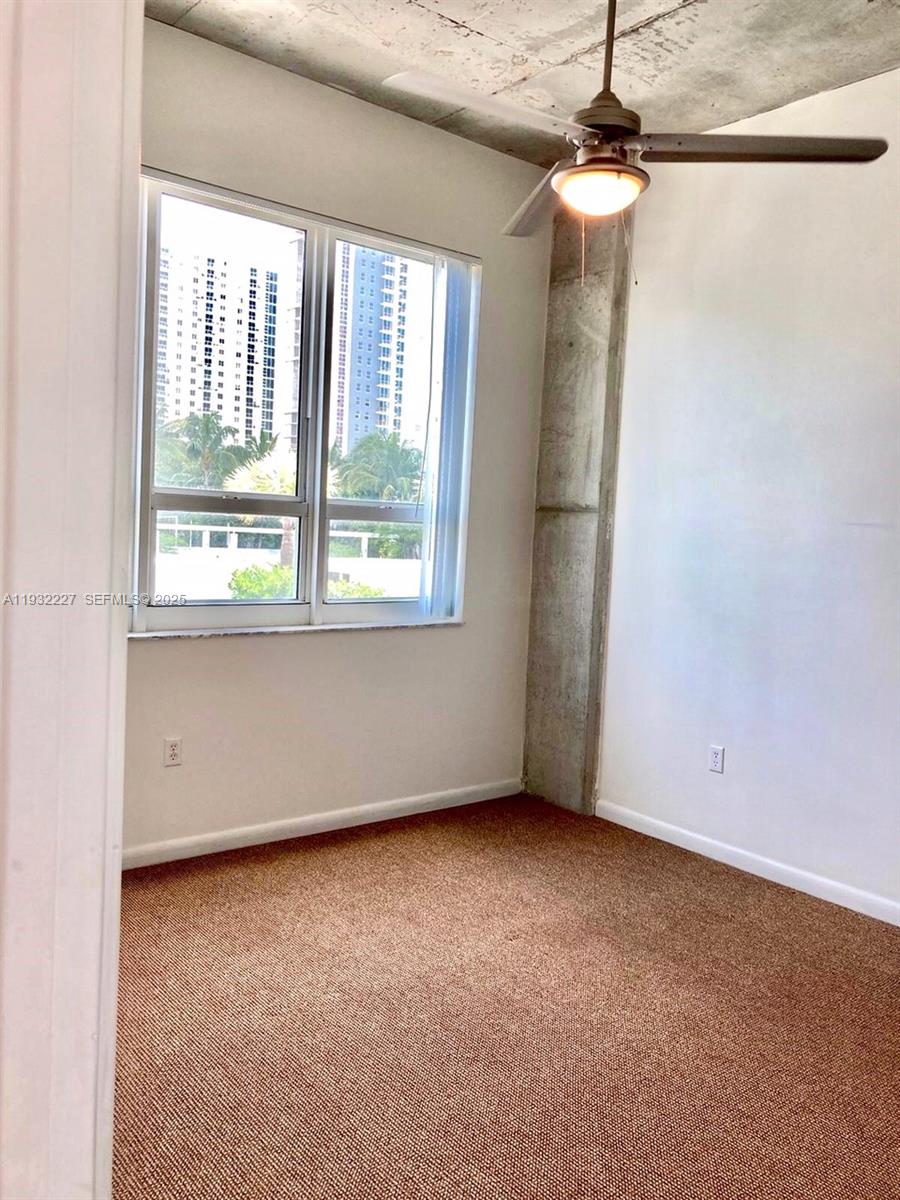 An empty room with brown carpet, a ceiling fan, and a window overlooking buildings — 2001 Biscayne Blvd # 2608, Miami FL 33137, MIAMI, FL