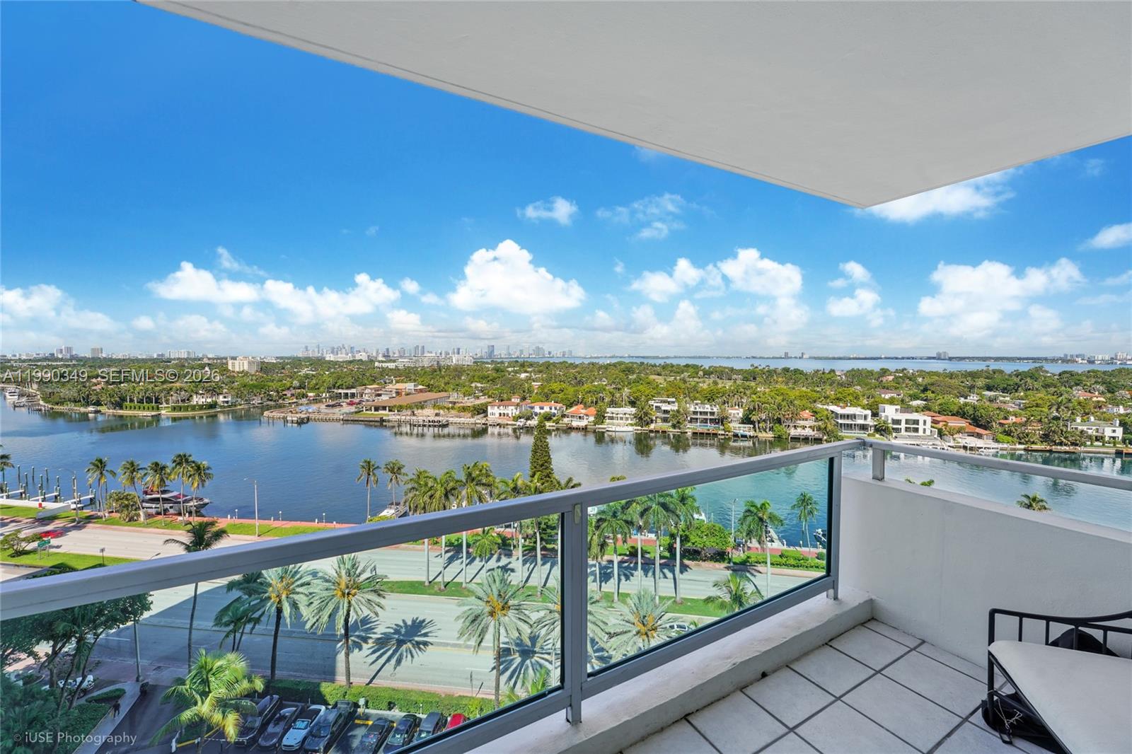 A high-rise balcony overlooks a waterway, palm trees, a road, and a distant city skyline — 5161 Collins Ave # 1508, Miami Beach FL 33140, MIAMI BEACH, FL