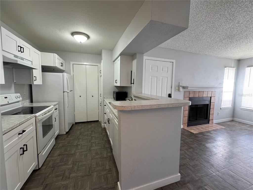 A kitchen with white cabinets, white appliances, and a breakfast bar overlooks a living area — 5540 DEVONBRIAR WAY UNIT 203, ORLANDO, FL