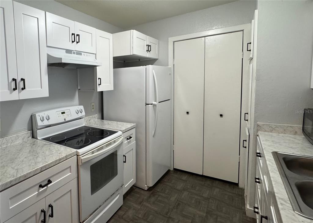 A kitchen features white cabinets, white appliances, and light-colored countertops with a marble pattern — 5540 DEVONBRIAR WAY UNIT 203, ORLANDO, FL