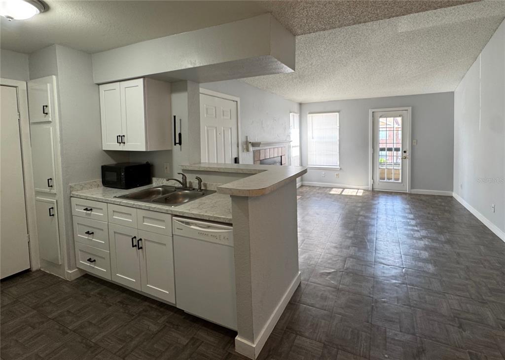 A kitchen with white cabinets and a dishwasher overlooks a living area with tile flooring — 5540 DEVONBRIAR WAY UNIT 203, ORLANDO, FL