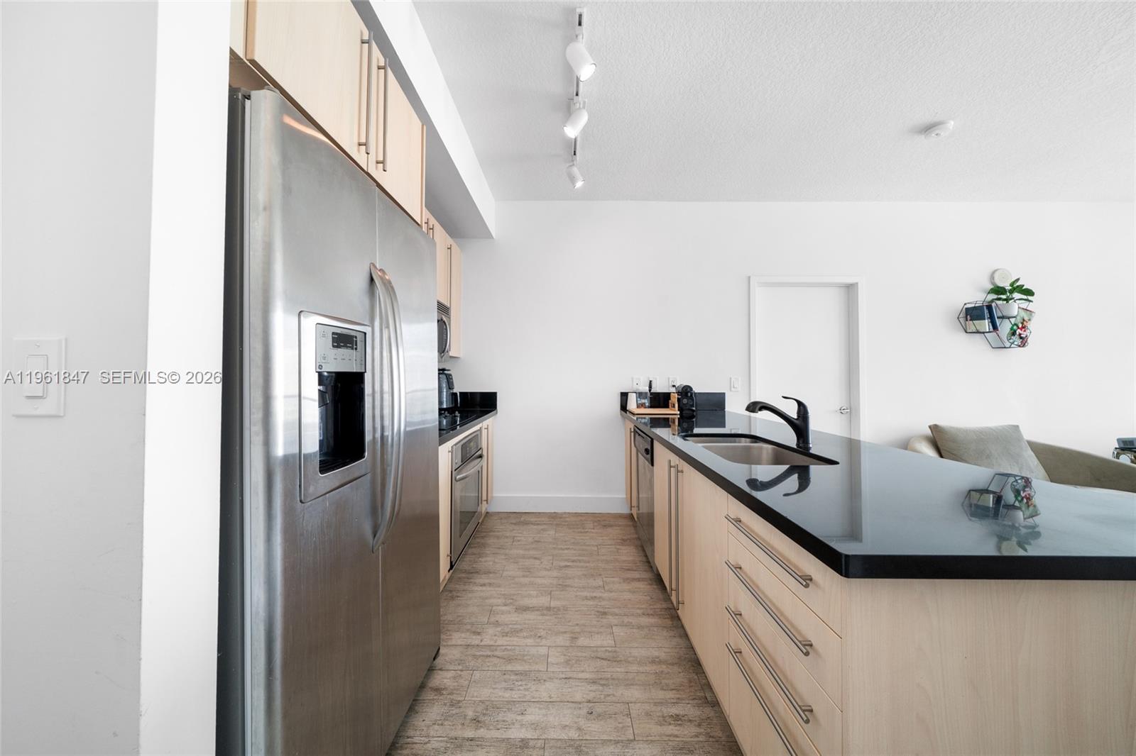 A kitchen features light wood cabinets, black countertops, stainless steel appliances, and wood-look flooring — 1111 SW 1st Ave, Miami FL 33130, MIAMI, FL