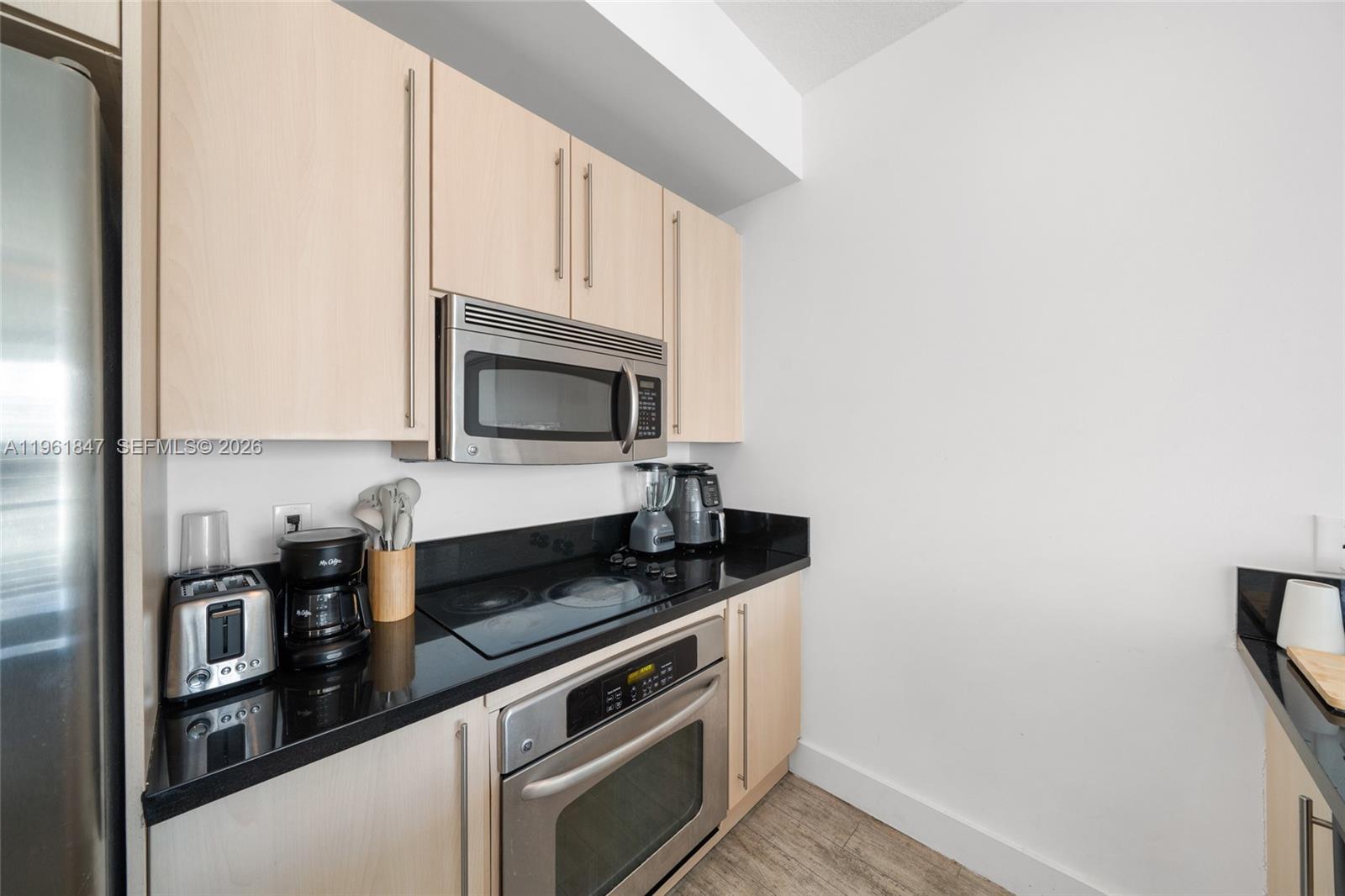 A kitchen features light wood cabinets, black countertops, and stainless steel appliances — 1111 SW 1st Ave, Miami FL 33130, MIAMI, FL