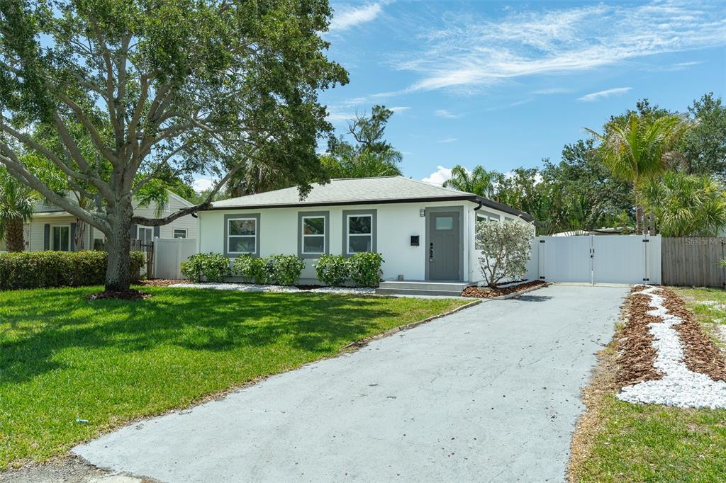 A single-story white house with a gray door, a paved driveway, and a large tree — 116 85TH AVENUE N, ST PETERSBURG, FL