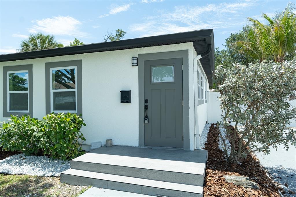 The exterior of a white house features a gray front door, steps, and landscaping — 116 85TH AVENUE N, ST PETERSBURG, FL