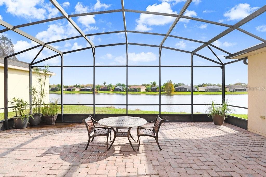 A screened-in patio with a brick floor features a small table and two chairs — 699 GLENDORA ROAD, KISSIMMEE, FL