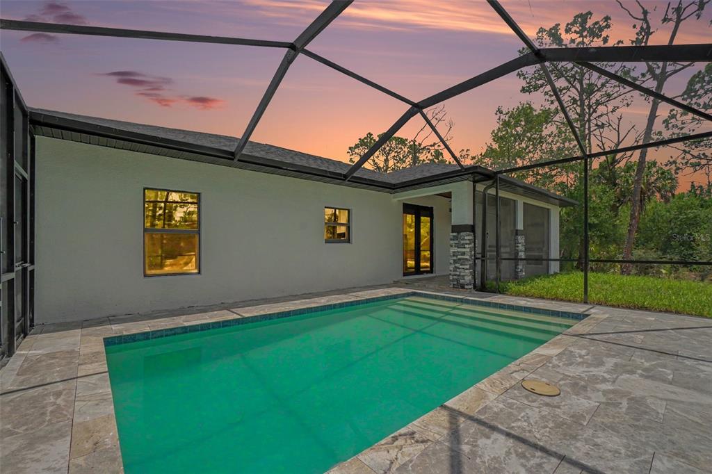 A swimming pool sits on a stone patio inside a screened-in outdoor enclosure — 1059 MADEIRA STREET, PORT CHARLOTTE, FL