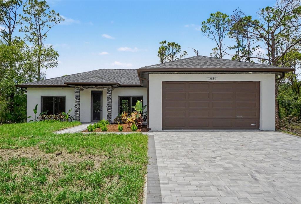 A single-story house with a white stucco exterior, stone accents, and a paved driveway — 1059 MADEIRA STREET, PORT CHARLOTTE, FL