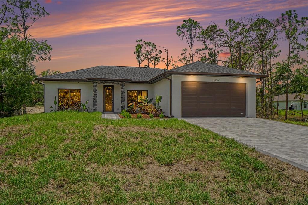 A single-story house with a stucco exterior, stone accents, and a two-car garage at dusk — 1059 MADEIRA STREET, PORT CHARLOTTE, FL