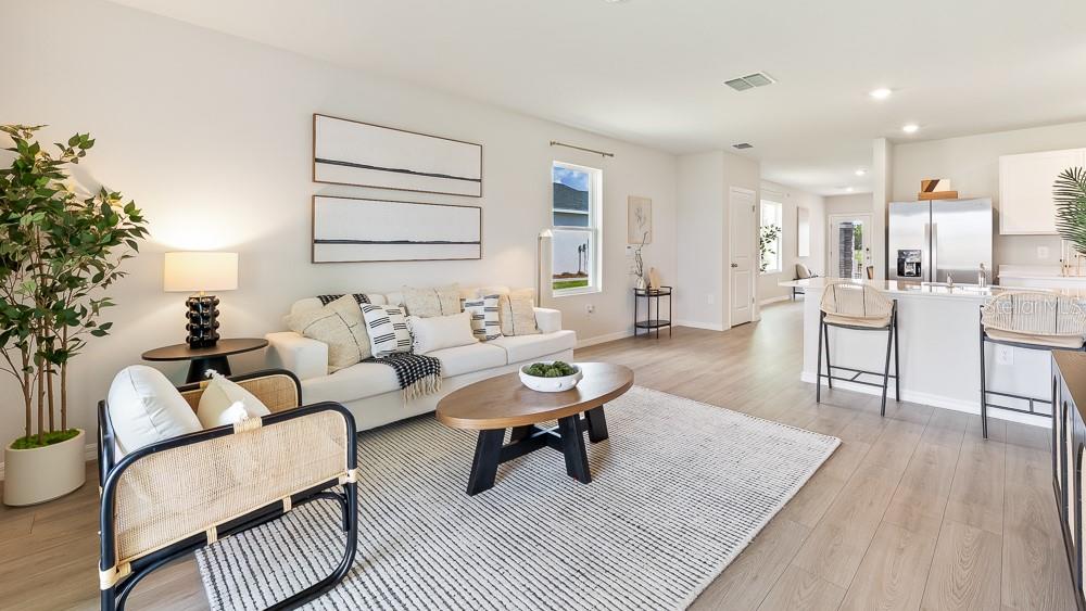 A bright living room features a white sofa, a wooden coffee table, and an open kitchen — 9956 MORNING MEADOWLARK TRAIL, PARRISH, FL