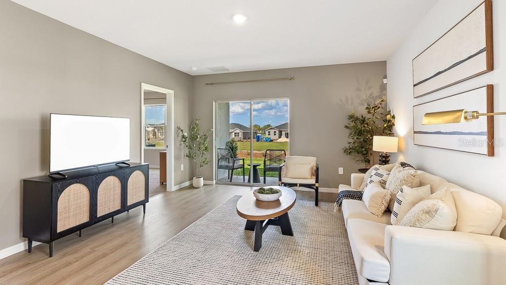 A living room features a white sofa, a black media console, and a sliding glass door — 9956 MORNING MEADOWLARK TRAIL, PARRISH, FL