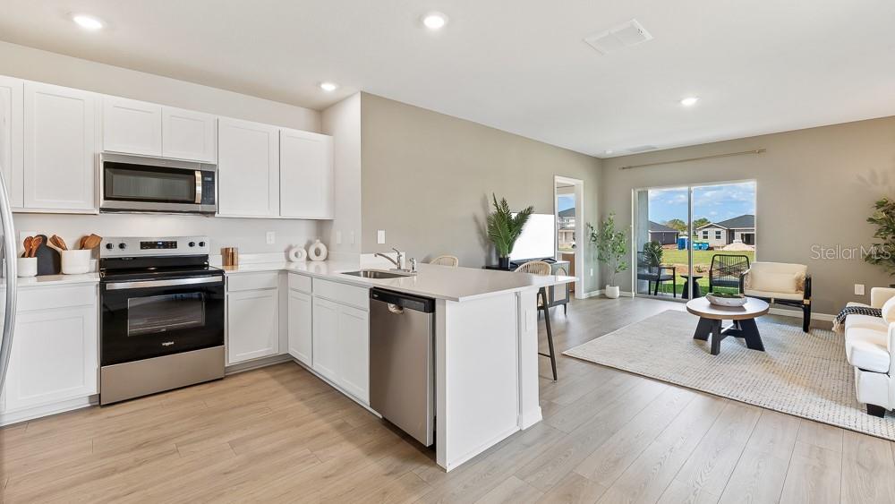 A modern kitchen with white cabinets and stainless steel appliances opens into a living area — 9956 MORNING MEADOWLARK TRAIL, PARRISH, FL