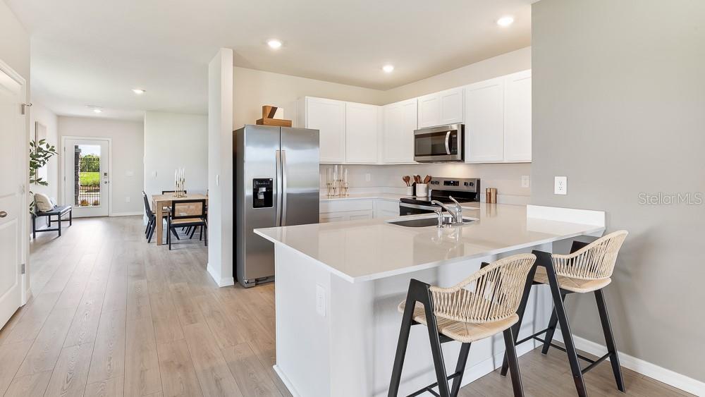 A modern kitchen features white cabinetry, stainless steel appliances, and a quartz-topped island with stools — 9956 MORNING MEADOWLARK TRAIL, PARRISH, FL