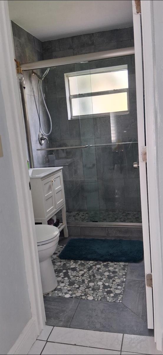 A small bathroom features a glass-enclosed shower, a white vanity, and gray tiled flooring — 1519 S 24th Terrace, Hollywood FL 33020, HOLLYWOOD, FL