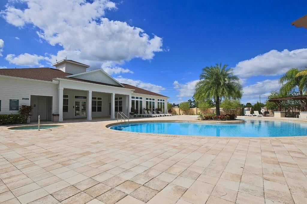 A swimming pool and hot tub sit on a paved patio beside a community clubhouse — 8905 SHINE DRIVE, KISSIMMEE, FL