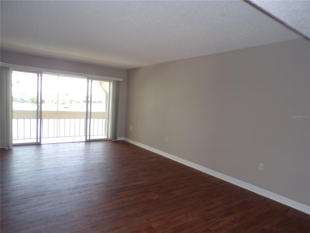 An empty living room features wood-look flooring, light gray walls, and a sliding glass balcony door — 1080 BAL HARBOR BOULEVARD UNIT 4D, PUNTA GORDA, FL