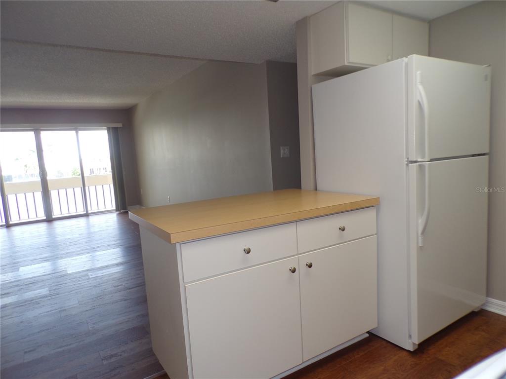 A kitchen island with a light wood countertop sits next to a white refrigerator — 1080 BAL HARBOR BOULEVARD UNIT 4D, PUNTA GORDA, FL