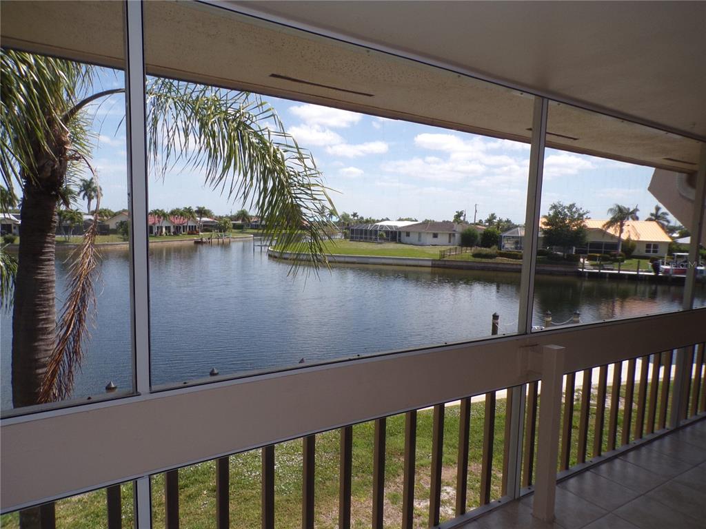 A screened-in porch overlooks a canal with houses and palm trees in the background — 1080 BAL HARBOR BOULEVARD UNIT 4D, PUNTA GORDA, FL