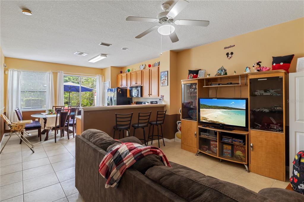 A living room with a brown sofa, entertainment center, and an adjacent kitchen with bar seating — 7646 LONG ISLAND DRIVE, KISSIMMEE, FL