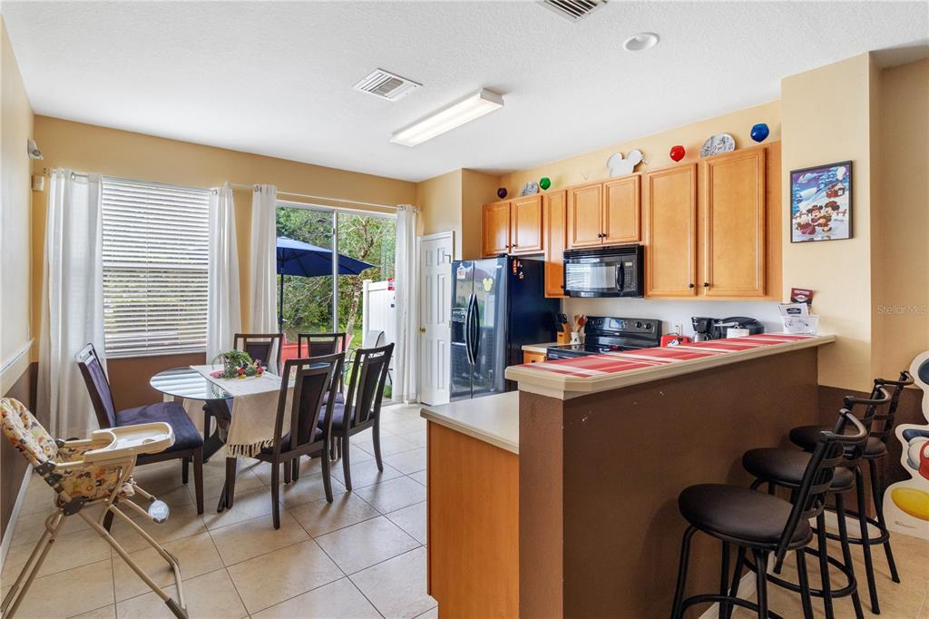 A kitchen with wood cabinets and a breakfast bar overlooks a dining area with sliding doors — 7646 LONG ISLAND DRIVE, KISSIMMEE, FL
