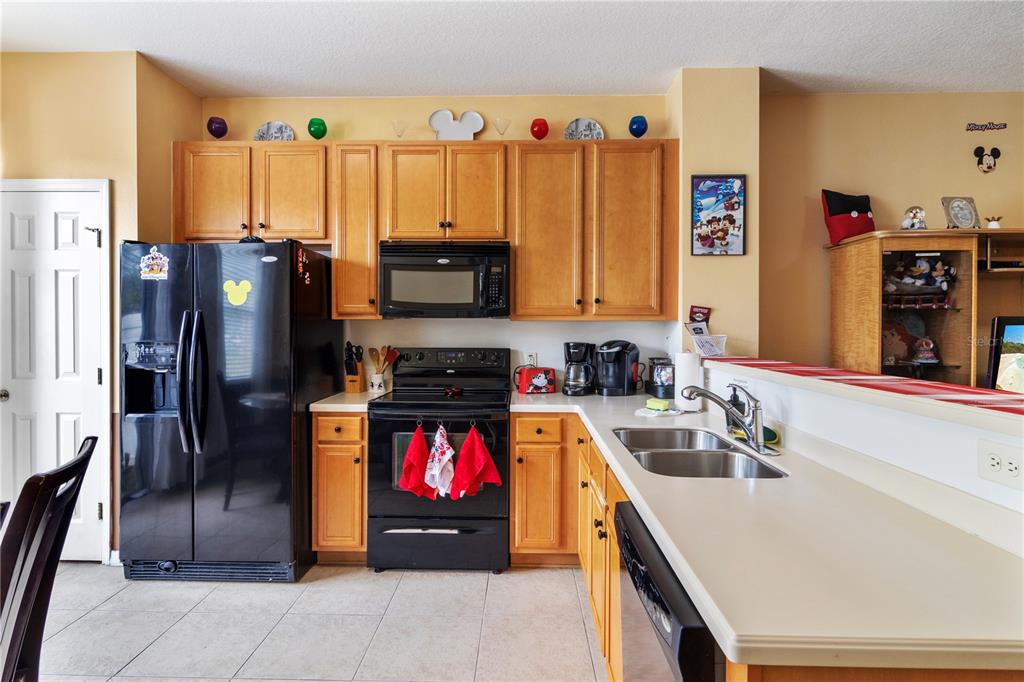 A kitchen features light wood cabinets, black appliances, and a white countertop with a sink — 7646 LONG ISLAND DRIVE, KISSIMMEE, FL