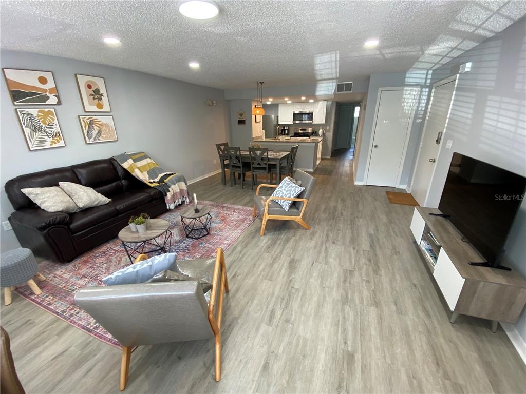 An open-concept living and dining area features wood-look flooring, a dark sofa, and modern furniture — 2723 N POINCIANA BOULEVARD UNIT 159, KISSIMMEE, FL