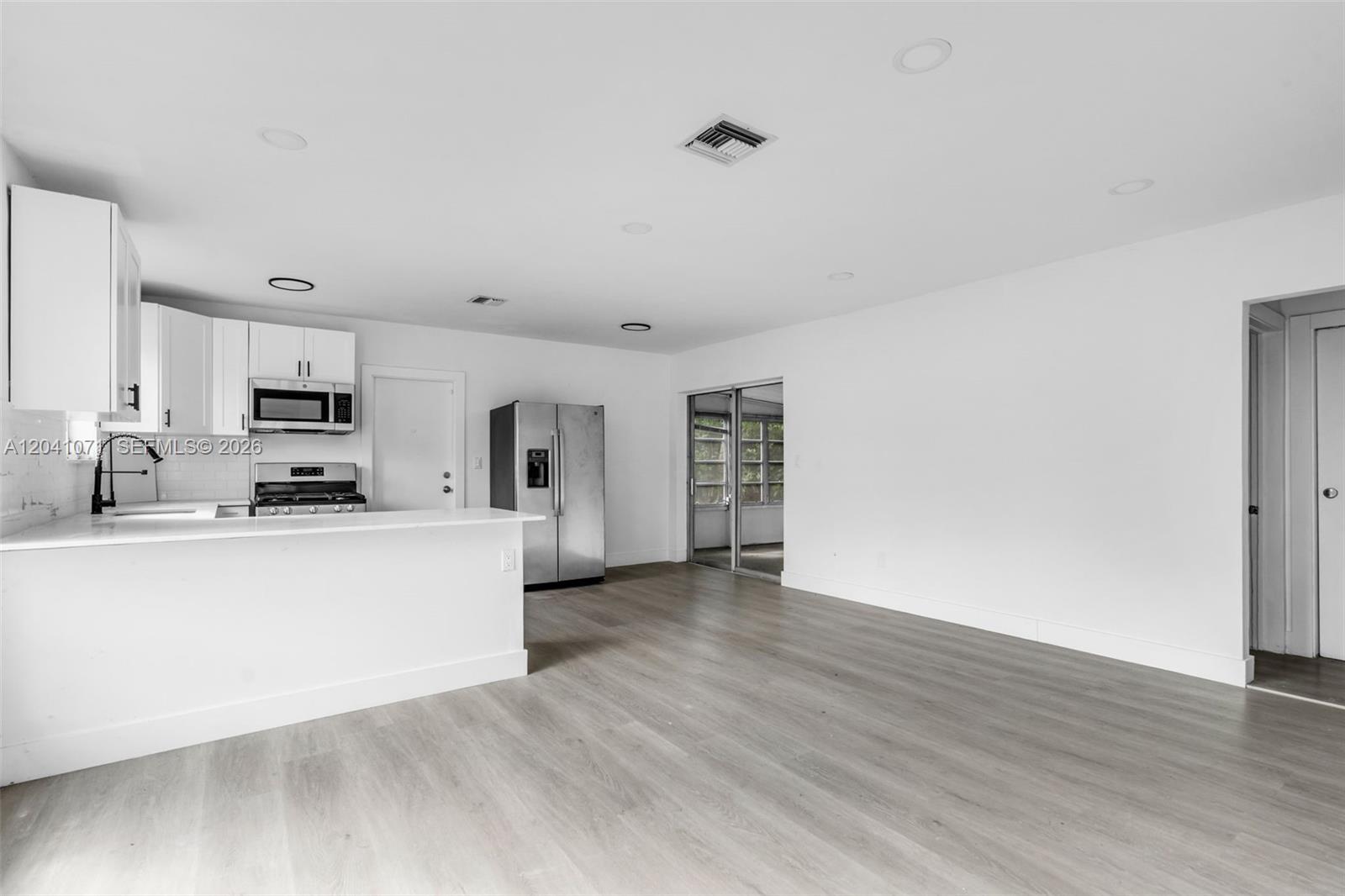 A kitchen with white cabinets and stainless steel appliances opens into a living area — 6831 Greene St # 6831, Hollywood FL 33024, HOLLYWOOD, FL