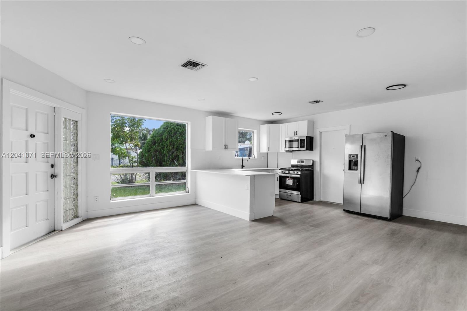 A kitchen and living area with white cabinets, stainless steel appliances, and light wood flooring — 6831 Greene St # 6831, Hollywood FL 33024, HOLLYWOOD, FL