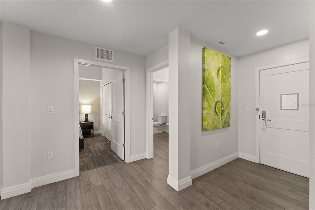 An interior hallway features light gray walls, wood-look flooring, two doorways, and a large leaf-themed artwork — 14501 GROVE RESORT AVENUE UNIT 2334, WINTER GARDEN, FL