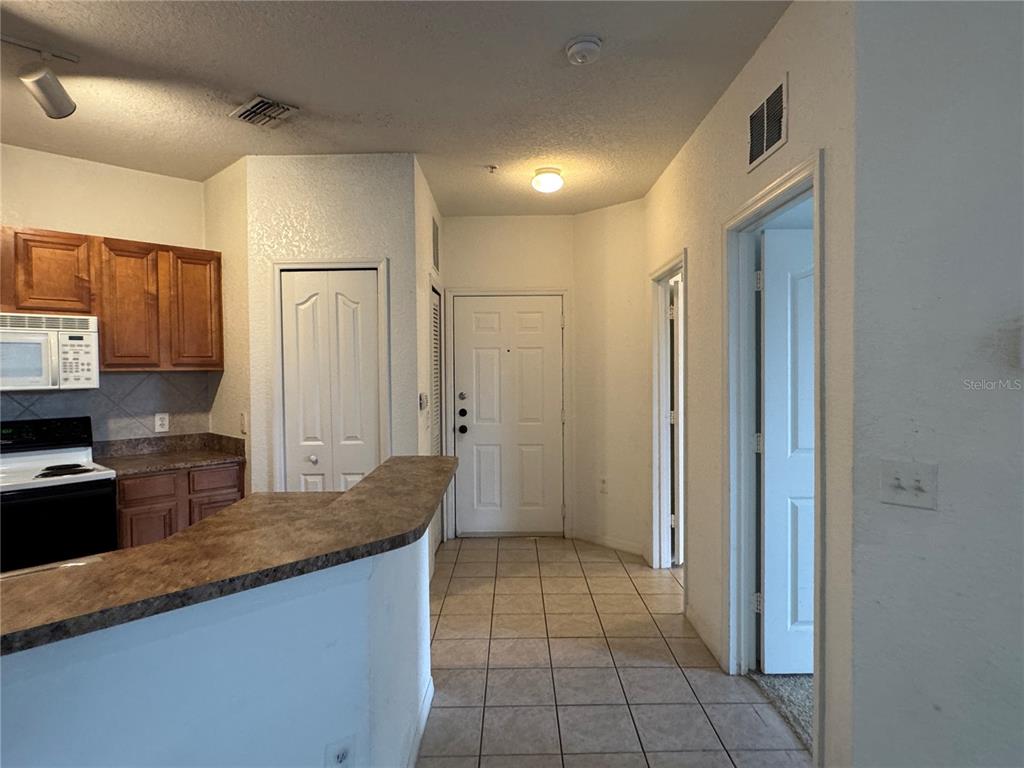 A kitchen with wood cabinets and a breakfast bar overlooks a tiled entryway — 6149 METROWEST BOULEVARD UNIT 208, ORLANDO, FL