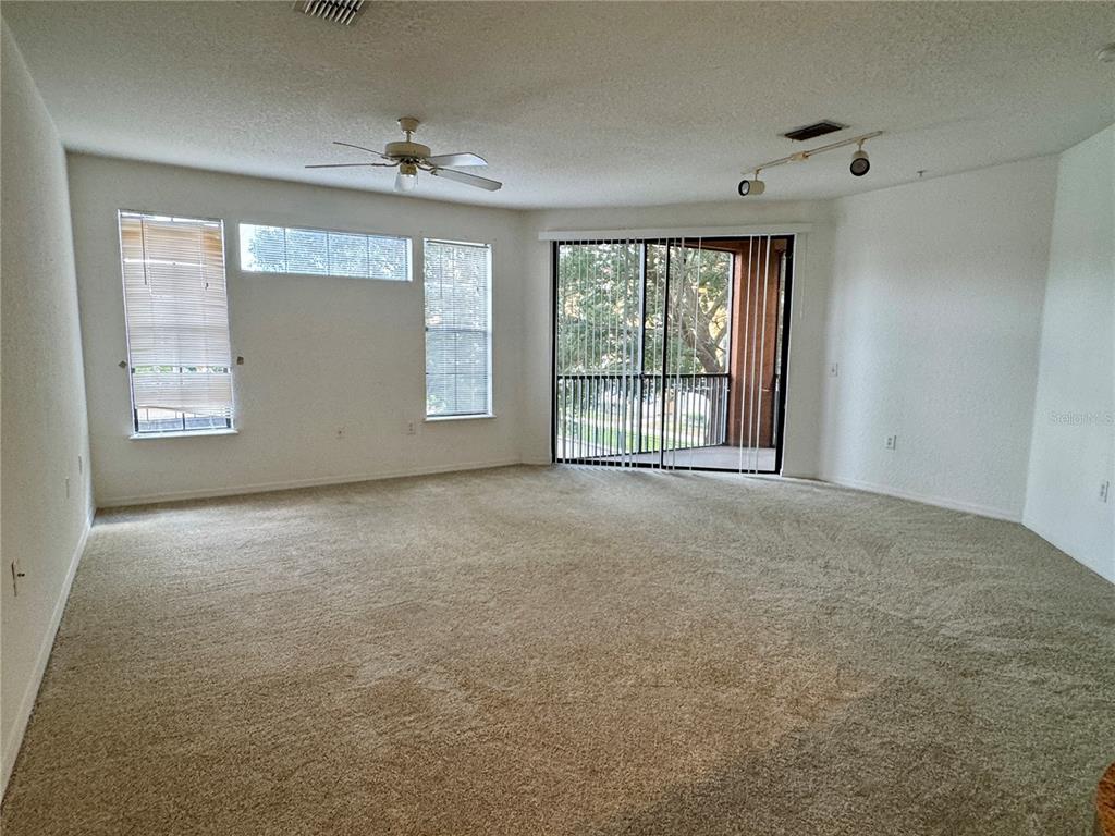 An empty living room features beige carpeting, a ceiling fan, track lighting, and sliding glass doors — 6149 METROWEST BOULEVARD UNIT 208, ORLANDO, FL
