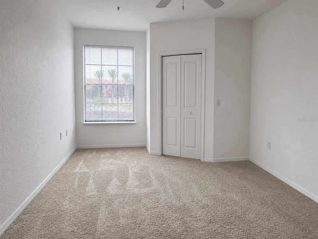 An empty bedroom features beige carpeting, white walls, a window with blinds, and a closet — 6149 METROWEST BOULEVARD UNIT 208, ORLANDO, FL