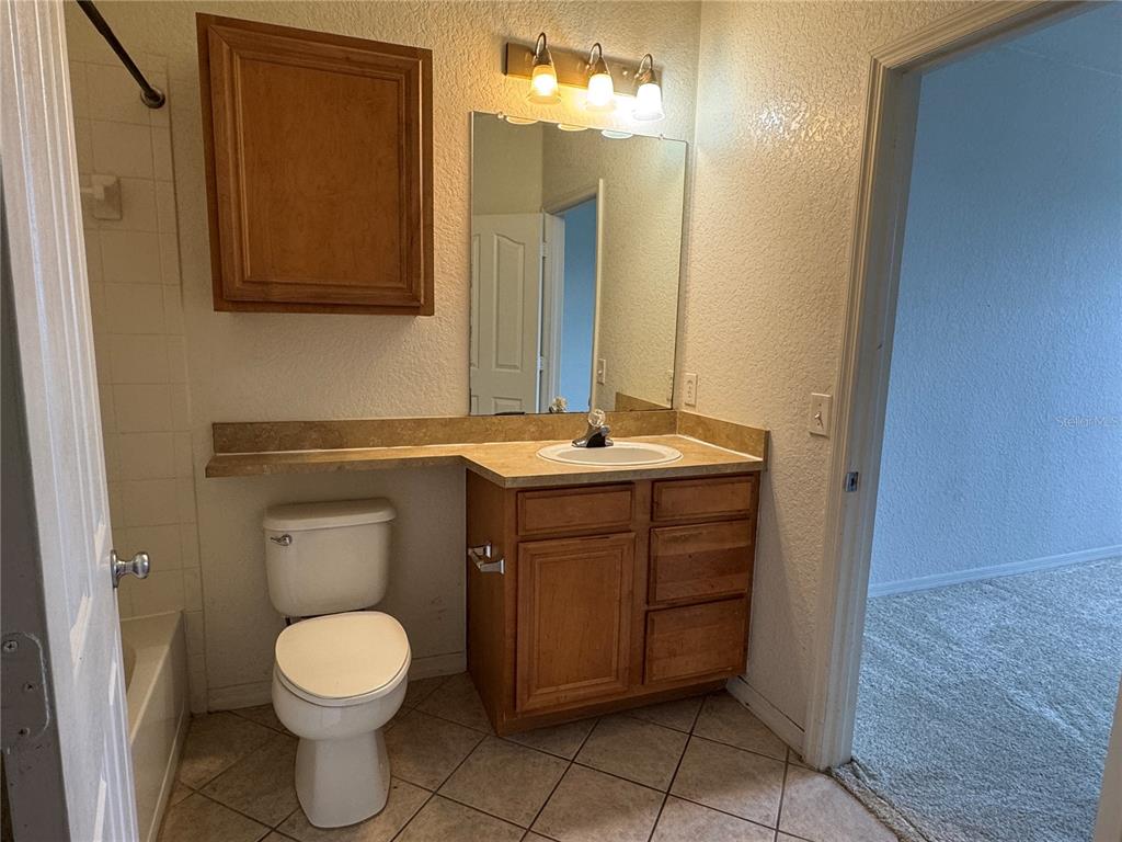 A bathroom features a wood vanity, a toilet, a mirror, and a shower-tub combination — 6149 METROWEST BOULEVARD UNIT 208, ORLANDO, FL