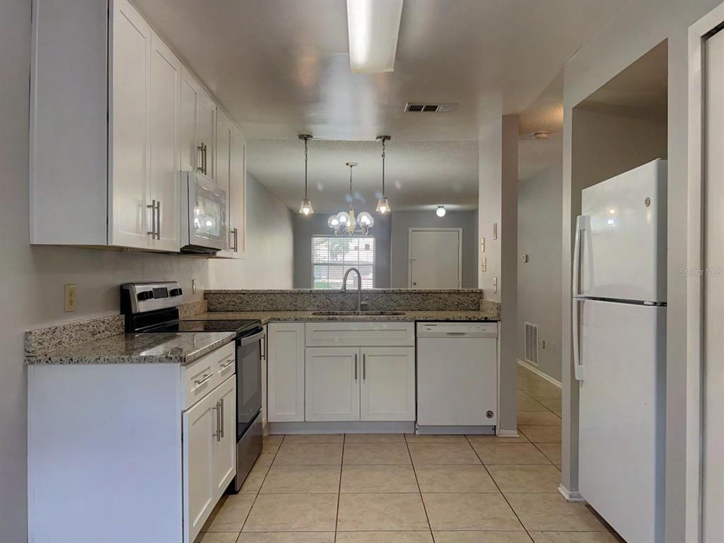 A kitchen with white cabinets, granite countertops, stainless steel appliances, and tile flooring — 1421 SOPHIE BOULEVARD, ORLANDO, FL