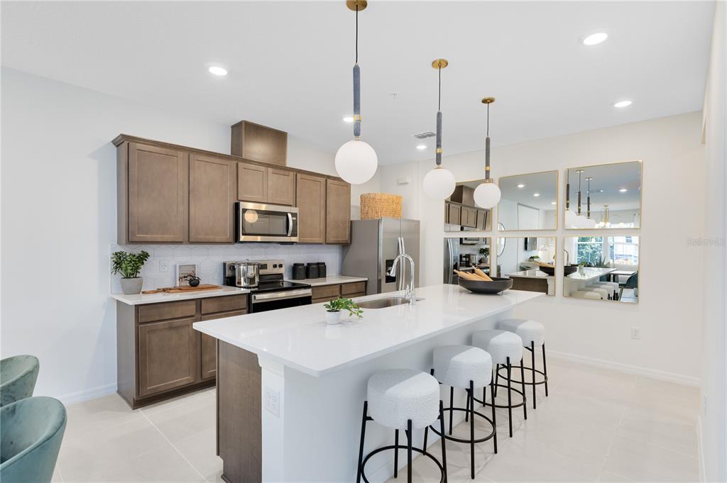 A modern kitchen features wood cabinets, a white quartz island, and three pendant lights — 11579 HARBORVIEW STREET, ORLANDO, FL