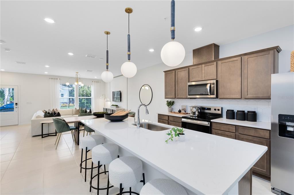 A modern kitchen features a white quartz island, brown cabinetry, and pendant lighting — 11579 HARBORVIEW STREET, ORLANDO, FL