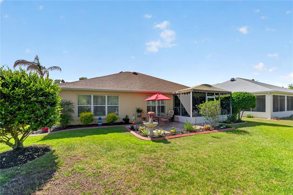 The backyard features a patio with a red umbrella, a fountain, and a screened enclosure — 9082 SE 120TH LOOP, SUMMERFIELD, FL