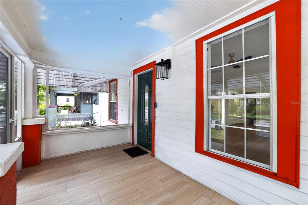 A covered porch with white siding, bright orange window trim, and light wood-look tile flooring — 813 E NEW ORLEANS AVENUE, TAMPA, FL