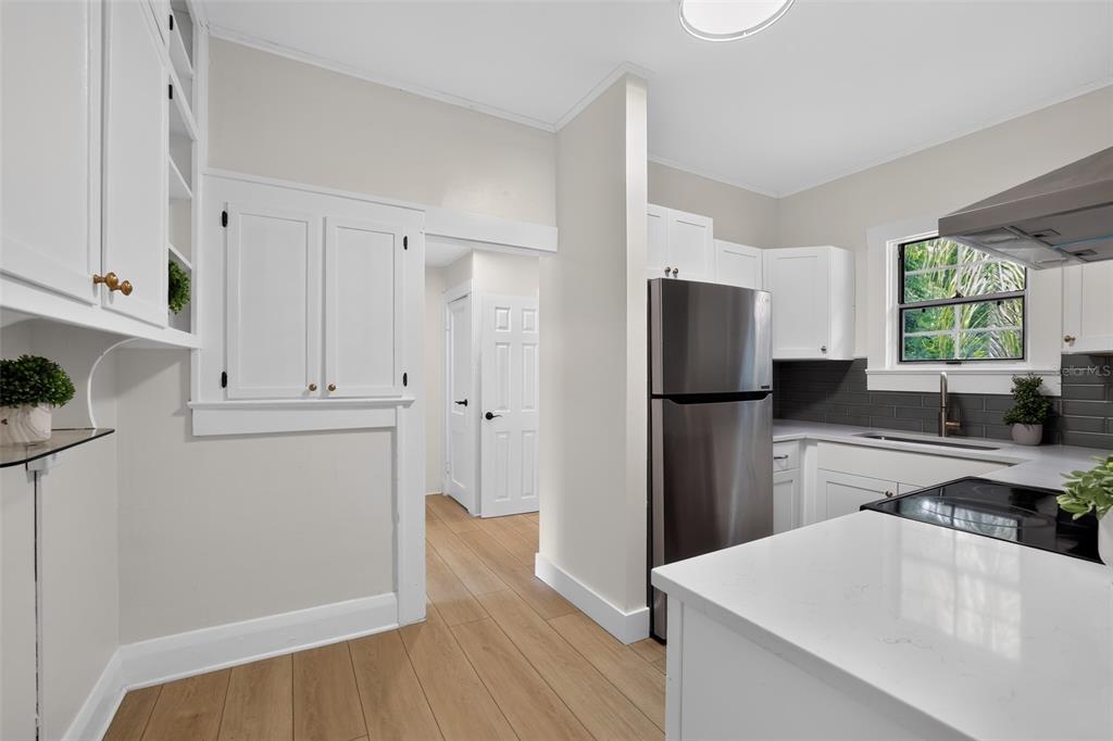 A kitchen features white cabinetry, a green tiled backsplash, and light wood-look flooring — 813 E NEW ORLEANS AVENUE, TAMPA, FL