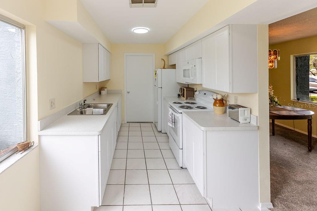 A galley-style kitchen features white cabinets, white appliances, and light-colored tile flooring — 7560 ST ANDREWS BOULEVARD UNIT 7560, WEEKI WACHEE, FL