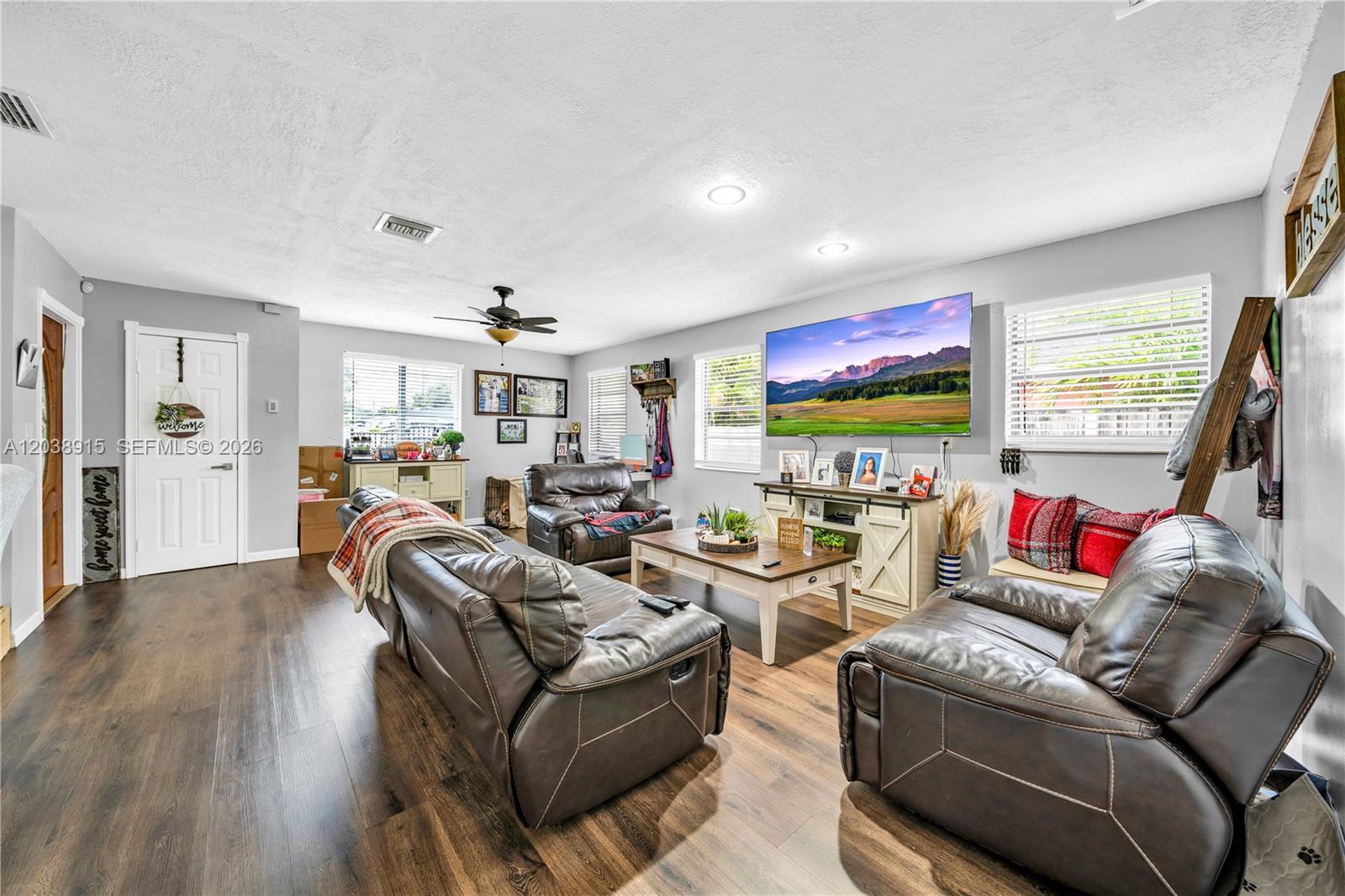 A living room features dark wood flooring, leather furniture, a wall-mounted television, and white walls — 875 E 29th St # 1, Hialeah FL 33013, HIALEAH, FL
