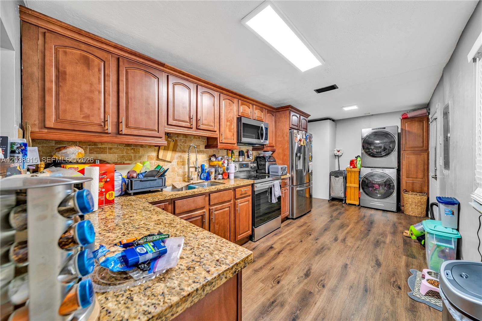 A kitchen features wood cabinets, granite countertops, stainless steel appliances, and a stacked laundry unit — 875 E 29th St # 1, Hialeah FL 33013, HIALEAH, FL