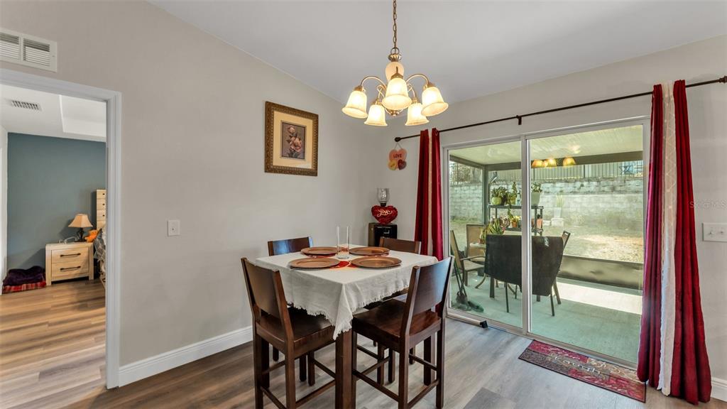 A dining area features a square table, wooden chairs, a chandelier, and sliding glass doors — 302 BROOKSHIRE DRIVE, LAKE WALES, FL
