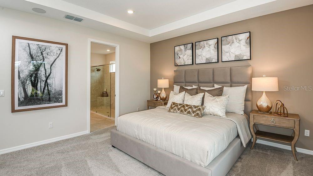 A bedroom features a tufted headboard, neutral walls, carpeted flooring, and an attached bathroom — 617 MOON SHELL CIRCLE, NEW SMYRNA BEACH, FL
