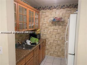 A kitchen features wooden cabinets, a stainless steel sink, a refrigerator, and patterned wallpaper — 4655 Palm Ave # 315, Hialeah FL 33012, HIALEAH, FL
