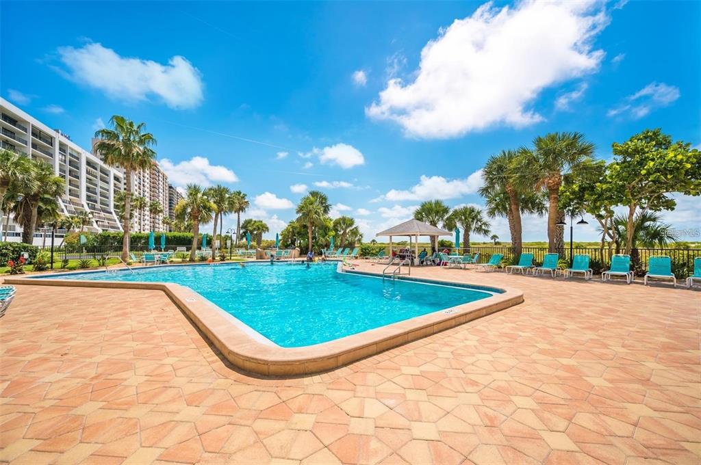 A swimming pool with a surrounding patio, lounge chairs, and palm trees under a blue sky — 1230 GULF BOULEVARD UNIT 1402, CLEARWATER BEACH, FL