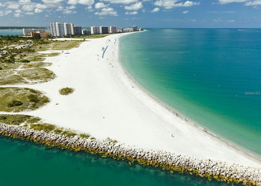 An aerial view shows a white sand beach, turquoise water, and a rocky jetty — 1230 GULF BOULEVARD UNIT 1402, CLEARWATER BEACH, FL