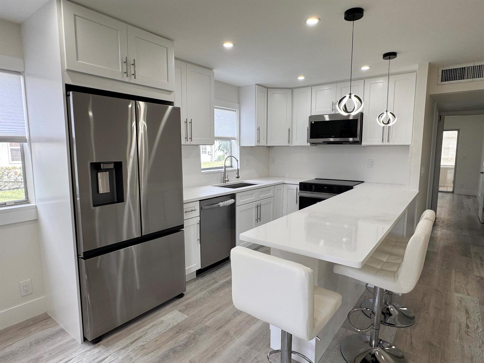 A modern kitchen features white cabinets, stainless steel appliances, and a white quartz breakfast bar — 108 Brittany # C, Delray Beach FL 33446, DELRAY BEACH, FL